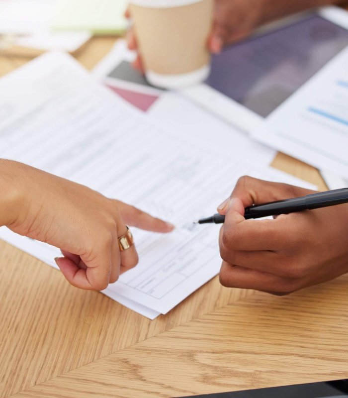 Closeup of two unknown ethnic business woman sitting and signing office contract. Mixed race profes.